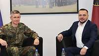 Ein Soldat sitzt neben einen Zivilisten. Beide posieren für ein Foto.