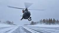 An H145M helicopter lands in a snowy landscape.