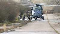 Soldaten verlassen einen gelandeten Hubschrauber und gehen in die nahen Büsche. 