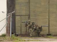 Zwei bewaffnete Soldaten stehen und hocken sichernd vor einem Hangartor.