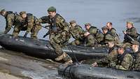 Zwei Schlauchboote mit mehreren Soldaten an einer Rampe im Wasser, ein Soldat springt aus dem Boot