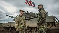 Ein deutscher und ein amerikanischer Soldat stehen vor einem Panzer und sprechen miteinander