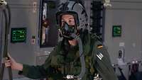 Ein Mann mit Uniform, Helm und Sauerstoffmaske steht in einem Flugzeug.