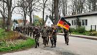 Soldatinnen und Soldaten marschieren zum Gedenken mit Flaggen durch Laage