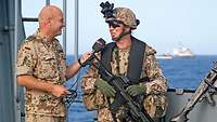 Ein Soldat in Gefechtsausrüstung wird auf einem Schiff von einem anderen Soldaten interviewt