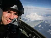 Ein Pilot mit Helm sitzt in einem Flugzeug. Im Hintergrund ist ein schneebedeckter Berg zu sehen.