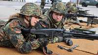 Mehrere Soldaten liegen nebeneinander auf Matten und halten Maschinengewehre in der Hand.