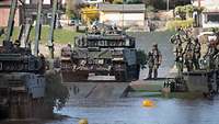 Mehrere Kampfpanzer vom Typ Leopard A7 befahren eine Schnellschwimmbrücke