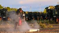 Ein Soldat löscht ein Feuer mit einem Feuerlöscher. Hinter ihm stehen mehrere Bundeswehrfahrzeuge.