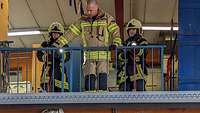 Zwei Mädchen in Feuerwehr-Schutzkleidung ziehen jeweils eine Schlauchrolle an einem Geländer hoch