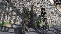 Zwei Soldaten stehen an einer Mauer mit Blickrichtung zum Gebäude