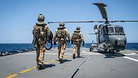 Three soldiers walk to the helicopter Sea Lynx on the flight deck of the frigate F 217 Bayern