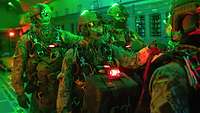 Soldatinnen und Soldaten mit Nachtsichtbrille stehen in grünlichem Licht in einem Laderaum