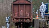 Soldatinnen und Soldaten in Ganzkörperanzügen untersuchen einen Bahnwaggon. 