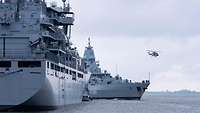 Ein graues Kriegsschiff fährt quer vor dem Bug eines großen grauen Schiffes