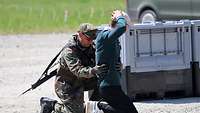 Ein Soldat tastet einen auf dem Boden knienden Mann auf Waffen ab
