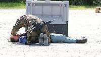 Ein Soldat kontrolliert an einer liegenden Person, ob die Atemwege frei sind