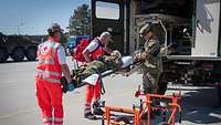 Ein Soldat hilft zwei Rettungssanitätern beim Verladen eines Verletzten in einen Krankenwagen