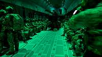 Kommandosoldaten sitzen im grün beleuchteten Frachtraum eines Transportflugzeugs