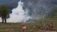 Ein Schützenpanzer fährt halb verdeckt von einer weißen Rauchwolke auf einer Wiese