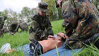 Soldaten üben auf einer Wiese an einer Puppe die Herz-Druck-Massage.