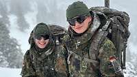 Zwei Soldatinnen in Winterausrüstung und mit Sonnenbrille in einer verschneiten Landschaft