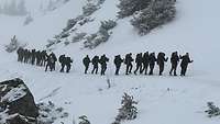 Eine Reihe von Soldaten mit Skistöcken und Schneetrittlingen in einer verschneiten Landschaft.
