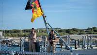 Zwei Marinesoldaten in sandfarbener Uniform stehen auf dem Oberdeck eines Schiffes.