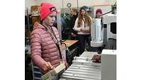 A young woman standing at a machine operating it with her right hand.