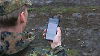Ein Soldat blickt auf ein Smartphone