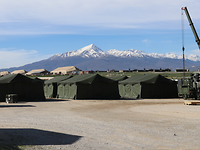 Vor einer Bergkulisse stehen grüne Bundeswehrzelte, im größeren Abstand dahinter große beige Zelte 