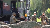 Vor einem Lkw der Bundeswehr stehen drei Soldaten, die das Fahrzeug beim Herumlaufen kontrollieren