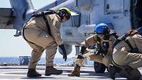 Marinesoldaten in Arbeitsuniform arbeiten neben einem grauen Hubschrauber auf einem Schiffsdeck