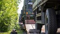 Auf einem Zug mit zahlreichen Waggons stehen militärische Lastkraftwagen.