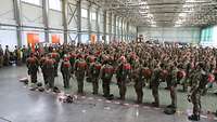 Hunderte Fallschirmjäger stehen in einer großen Halle in Reih und Glied.