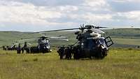 Auf einem Feld stehen Soldaten bei jeweils verschiedenen Hubschraubern