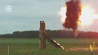Ein Lenkflugkörper steuert auf einen Stahlträger auf einem Feld zu und explodiert