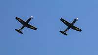 Zwei Propellerflugzeuge von unten vor einem blauen Himmel fotografiert.