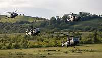 Vier Hubschrauber sind im Landeanflug auf eine Wiese