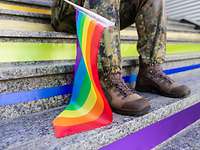 Eine Soldatin sitzt auf einer bunt beklebenden Treppe und hält eine Regenbogenflagge
