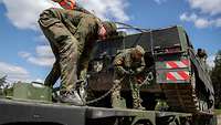 Zwei Soldaten zurren einen Panzer auf einem Schwerlasttransporter mit Stahlketten fest.