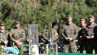 Zwei Kerzen, ein Parament und ein Kreuz, im Hintergrund Soldaten, die dem Feldgottesdienst besuchten