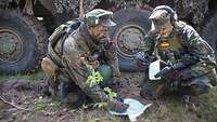Zwei Soldaten knien vor dem Transportpanzer Fuchs auf dem Boden und schauen auf die Karte