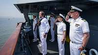 Marinesoldaten in weißer Uniform stehen auf dem Deck eines Schiffes und grüßen militärisch.