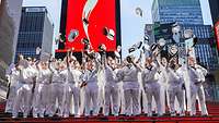 A large group of sailors in white uniforms throw their caps in the air.