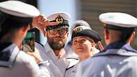 A male and female Marine in white uniforms pose for a cell phone photo.