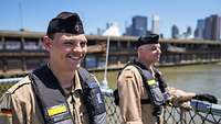 Two marines in sand-colored work uniforms smile brightly.