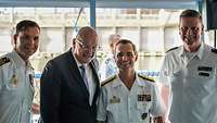 Three naval officers in white uniforms and a man in a suit and tie.