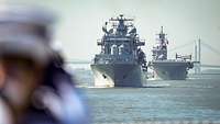 Two large gray ships in motion, a large bridge in the background.