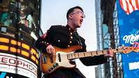 A soldier in a dark blue uniform plays the electric guitar.